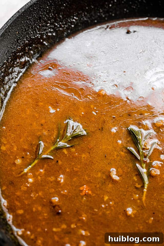 Sticky Apple Cider Chicken Thighs 5 A close-up shot of the apple cider Dijon glaze bubbling and reducing in a black cast-iron skillet, with a wooden spoon stirring it.