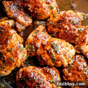 Sticky Apple Cider Chicken Thighs 7 An overhead shot of savory apple cider glazed chicken thighs resting in a black cast-iron skillet, garnished with fresh herbs.