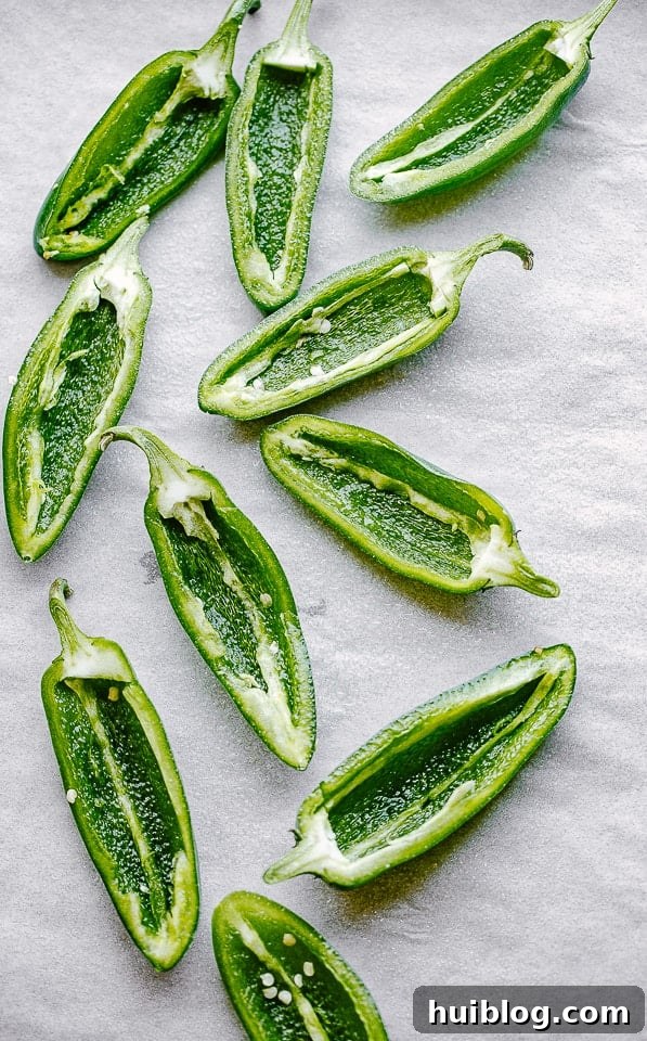 Bacon Jalapeno Delights 3 Halved and seeded fresh jalapeños are neatly arranged on a parchment-lined baking surface, ready for stuffing.