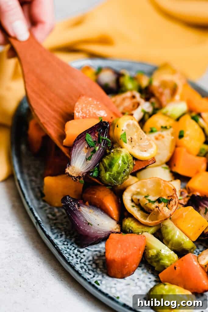 A wooden spoon scooping roasted vegetables off a blue platter.