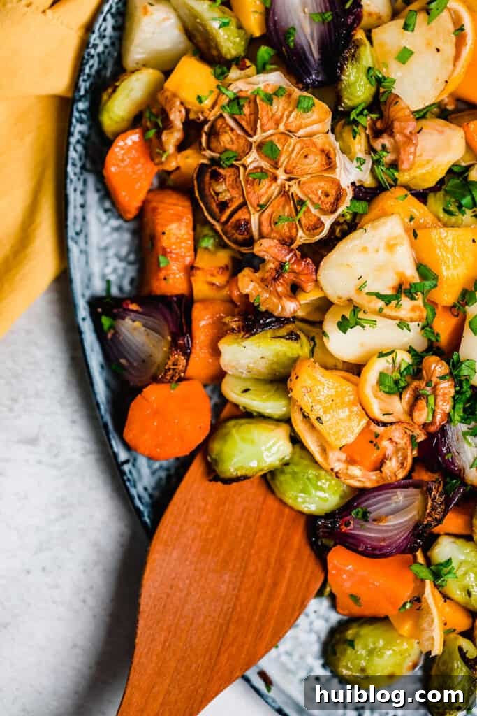 A wooden spoon resting on roasted vegetables on a blue platter.