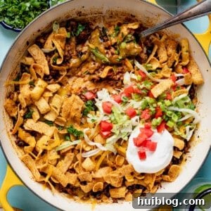Skillet with walking taco casserole in it, topped with shredded lettuce, sour cream, and diced tomato.