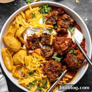 Bowl of meatball chili served with Fritos, grated cheese, and sour cream.