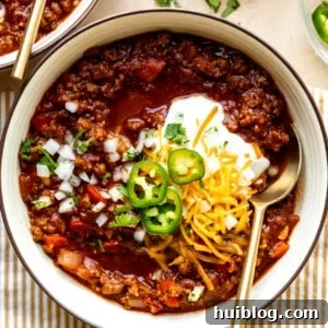 Bowl of ground beef Texas Chili topped with sour cream, sliced jalapeños, and shredded cheese.