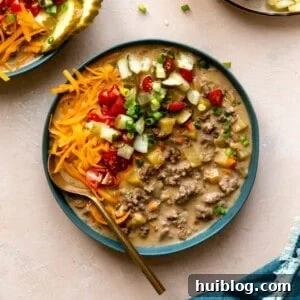 Bowl filled with cheeseburger soup and topped with diced tomatoes, pickles, cheese and herbs.