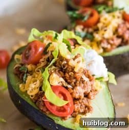 Close up of halved avocado stuffed with taco meat, cheese, lettuce, tomato and sour cream.