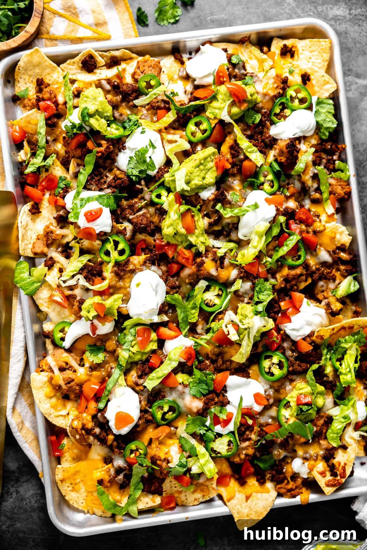 Sheet pan nachos with ground beef topped with sour cream and guacamole.
