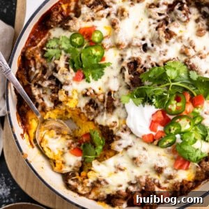 White baking dish with tamale pie topped with melted cheese, sliced jalapeno, diced tomatoes, sour cream and cilantro.