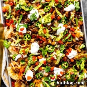 Sheet pan nachos with ground beef topped with sour cream and guacamole.