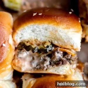 Up close cheeseburger slider on hawaiian rolls showing layers of ground beef, cheese, pickles and burger sauce.
