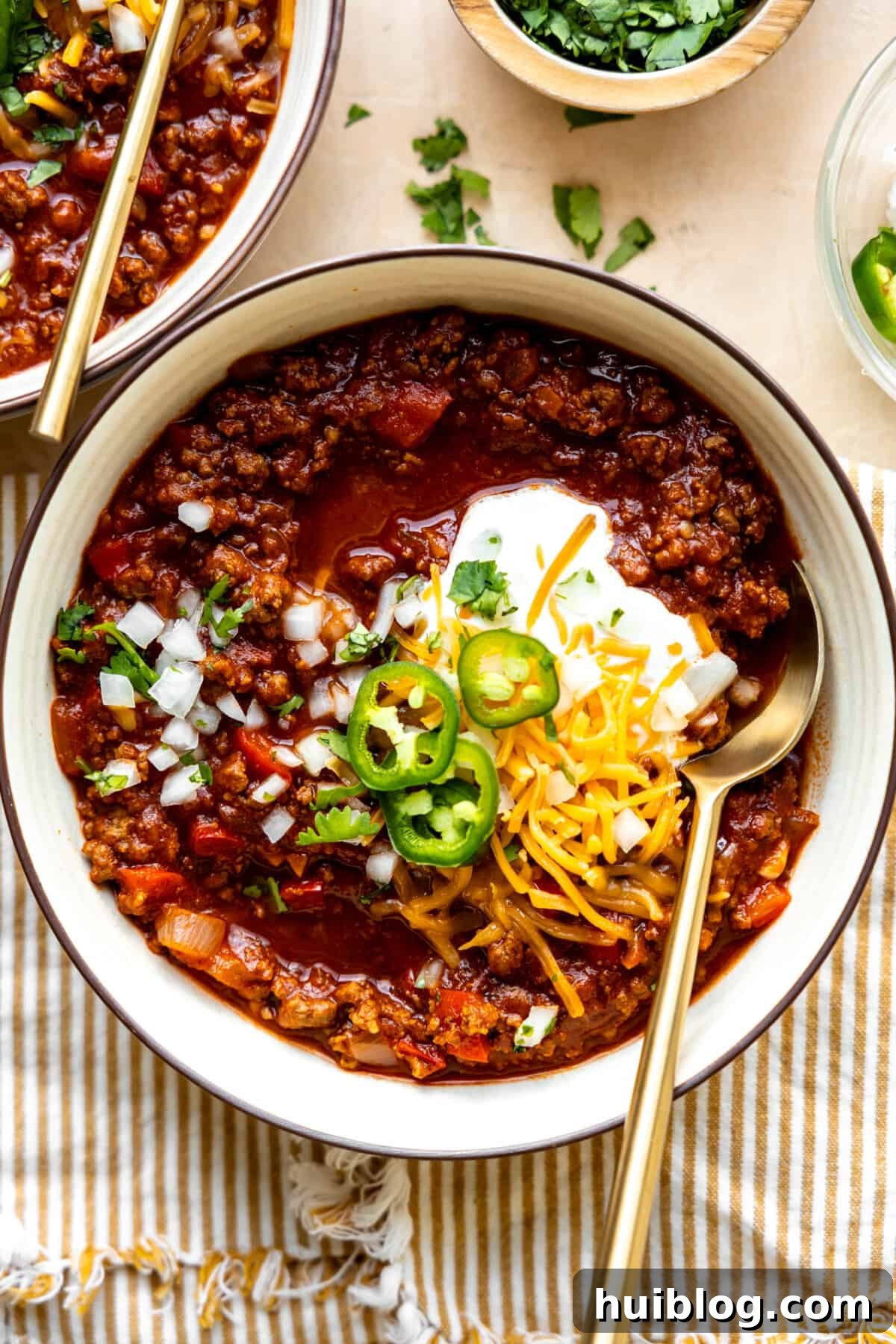 Bowl of ground beef Texas Chili topped with sour cream, sliced jalapeños, and shredded cheese.