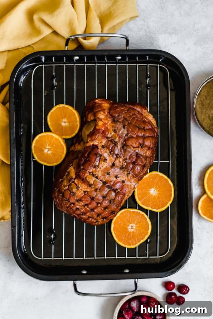 A Christmas Ham on a Roasting Pan with Four Orange Slices, adding a fresh, citrusy aroma.