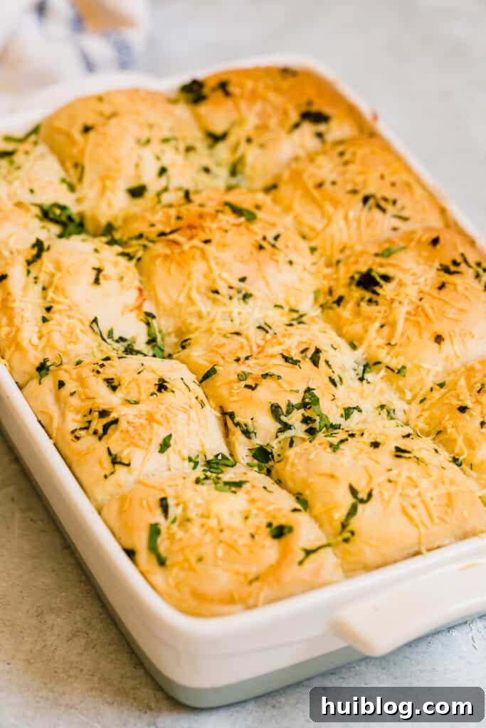 Twelve golden-brown Soft Parmesan Dinner Rolls in a baking pan, fresh from the oven, ready to be served on a countertop.