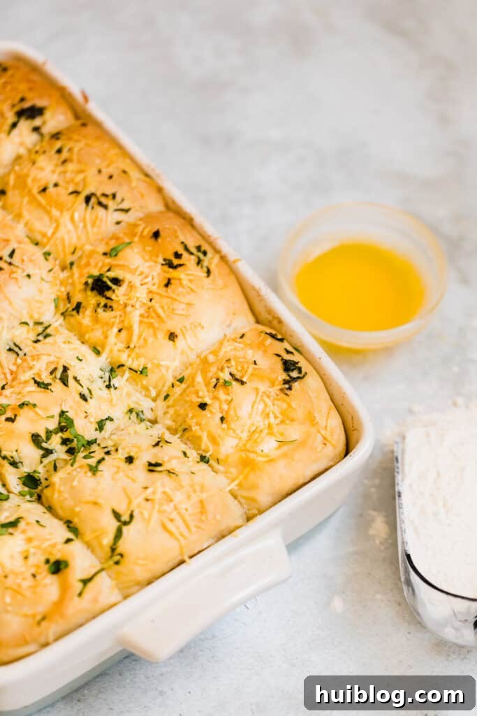 A pan filled with golden-brown Soft Parmesan Dinner Rolls, highlighting their perfectly baked exterior and savory topping of cheese and parsley.