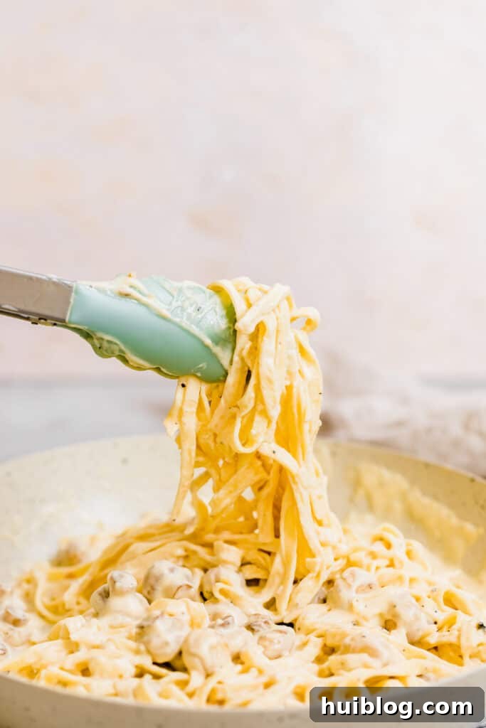 Velvety Chicken Fettuccine Alfredo 4 A Pair of Tongs Grabbing a Bunch of Fettuccine Noodles Covered in Alfredo