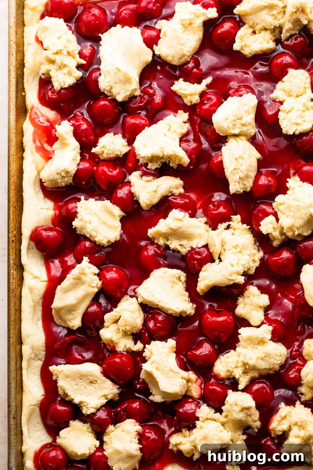 Scoops of Kuchen Dough Overtop Cherry Pie filling in a baking pan