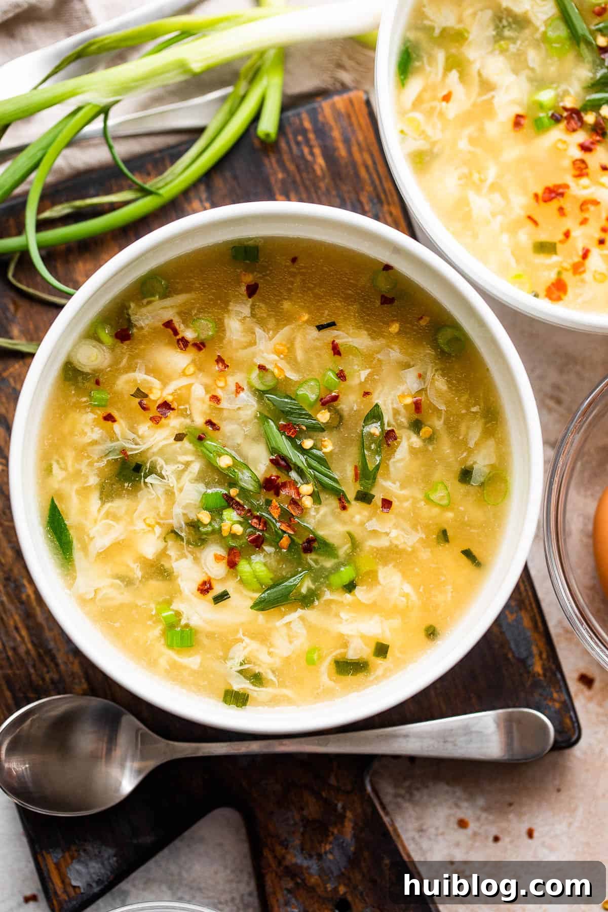 Two white bowls filled with golden egg drop soup, garnished with vibrant green onions, sit ready to be enjoyed.