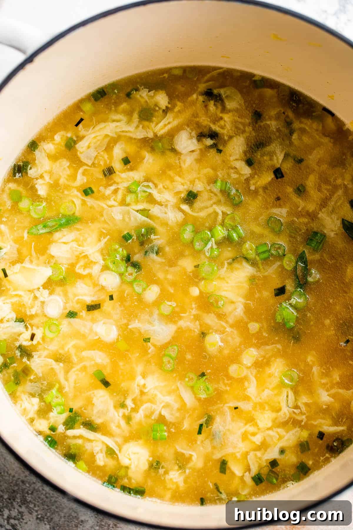 Egg drop soup simmering gently in a large Dutch oven on a stovetop, showing the development of soft egg ribbons.