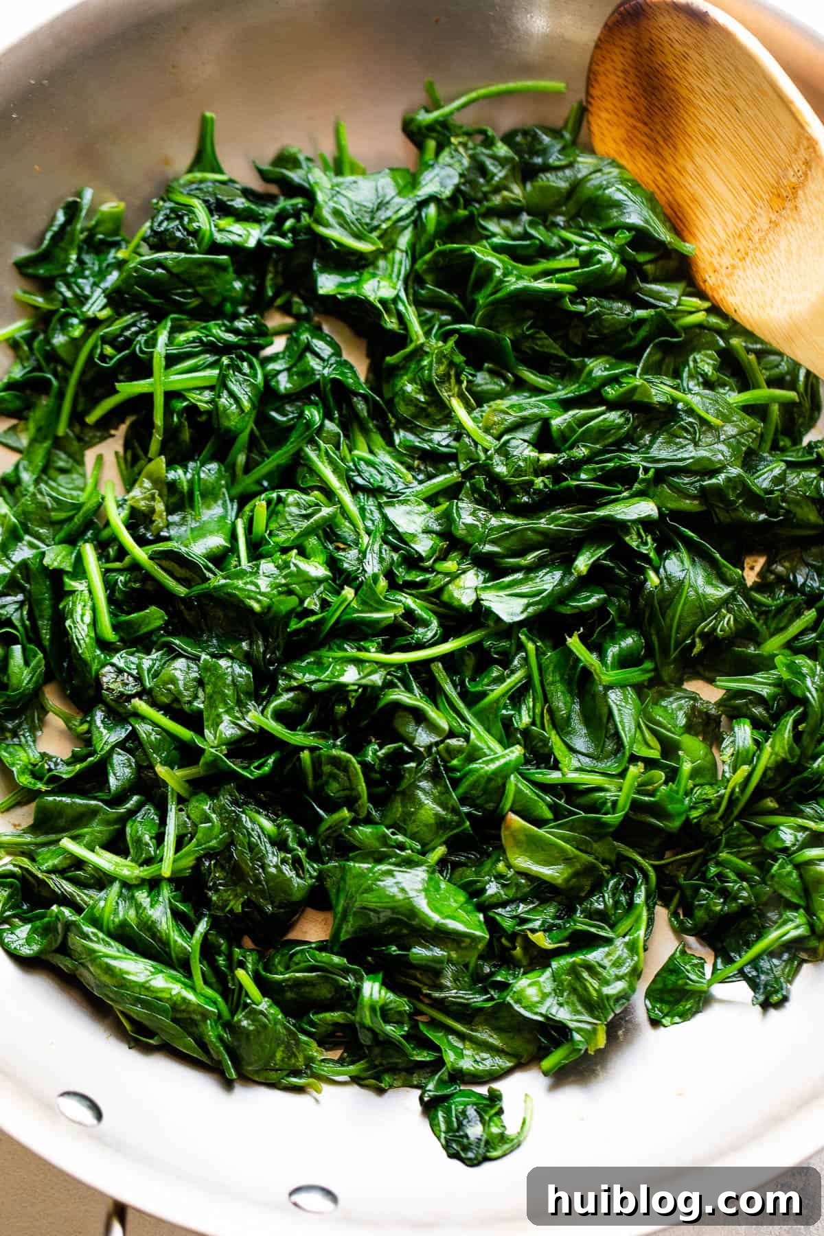 Fresh baby spinach being wilted in a stainless steel skillet with olive oil, preparing it for the creamy sauce.