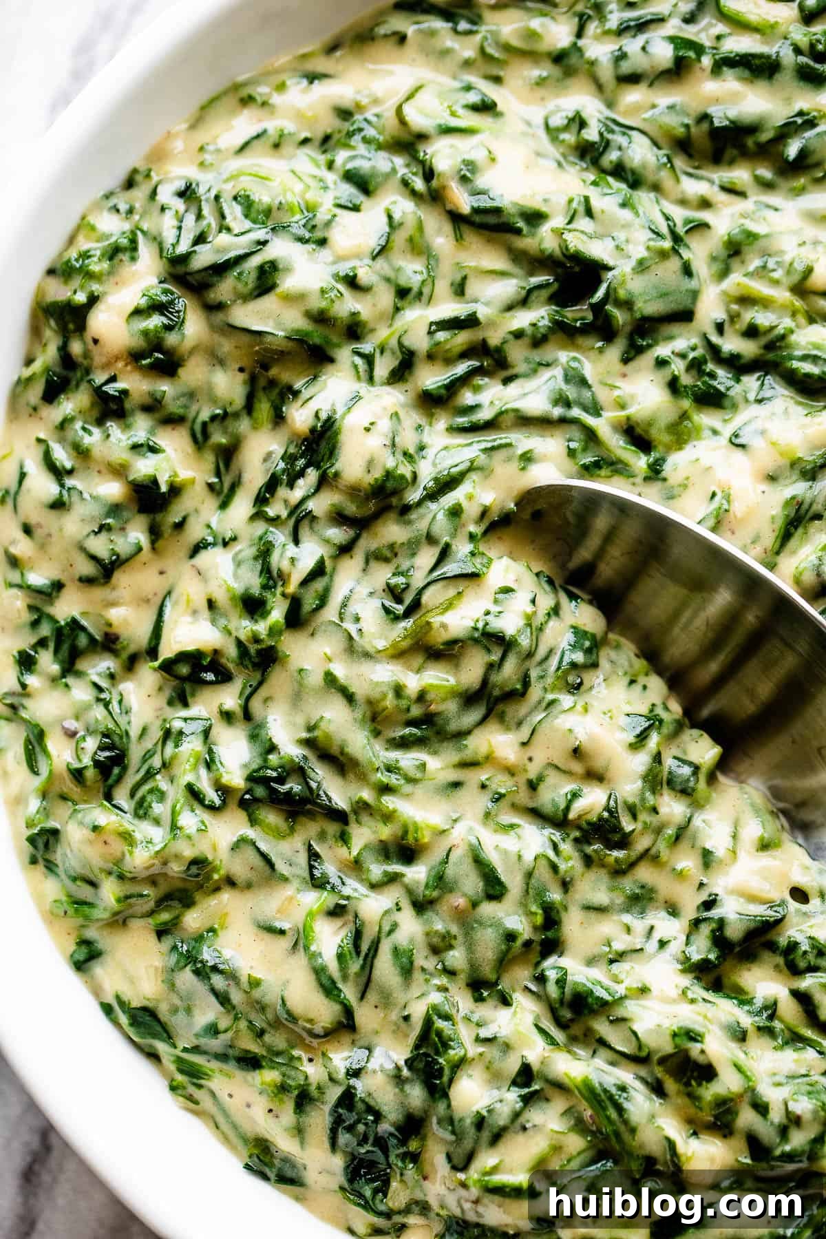 A white bowl filled with creamy steakhouse creamed spinach, garnished with a spoon, ready for serving.