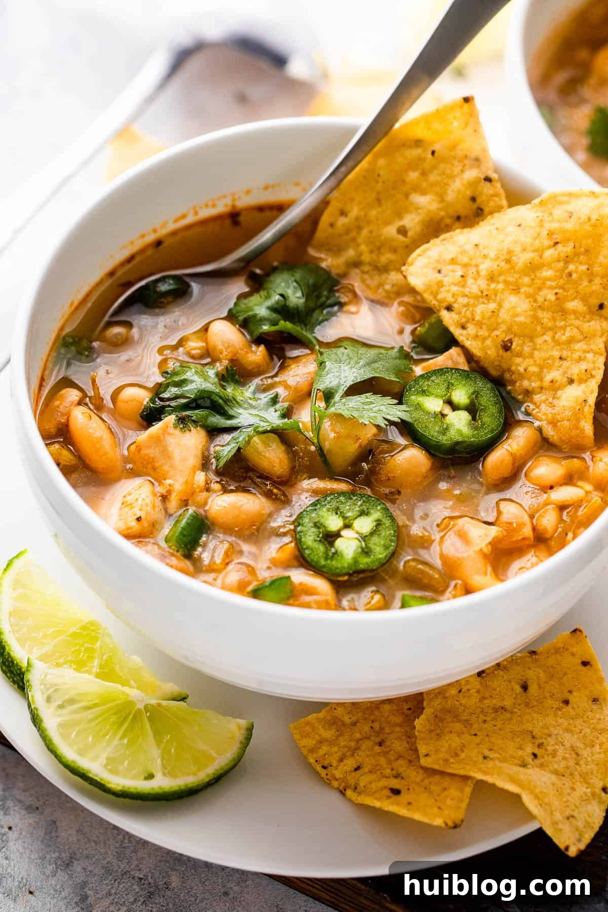 Close-up of a bowl of homemade Chicken Chili garnished with fresh jalapeños and crispy tortilla chips.