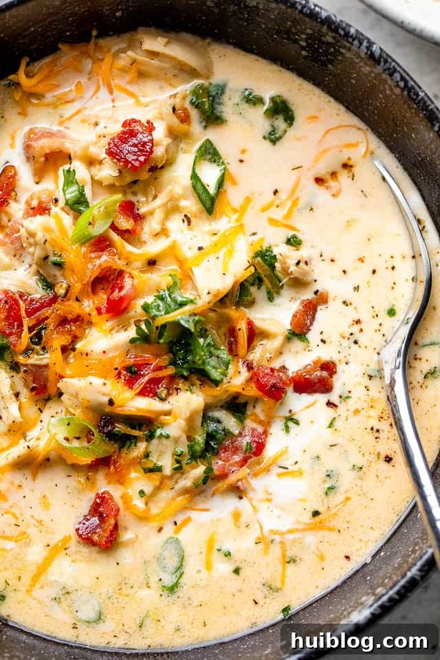 A hearty bowl of Slow Cooker Crack Chicken Soup garnished with crispy bacon, fresh scallions, and shredded cheddar cheese.