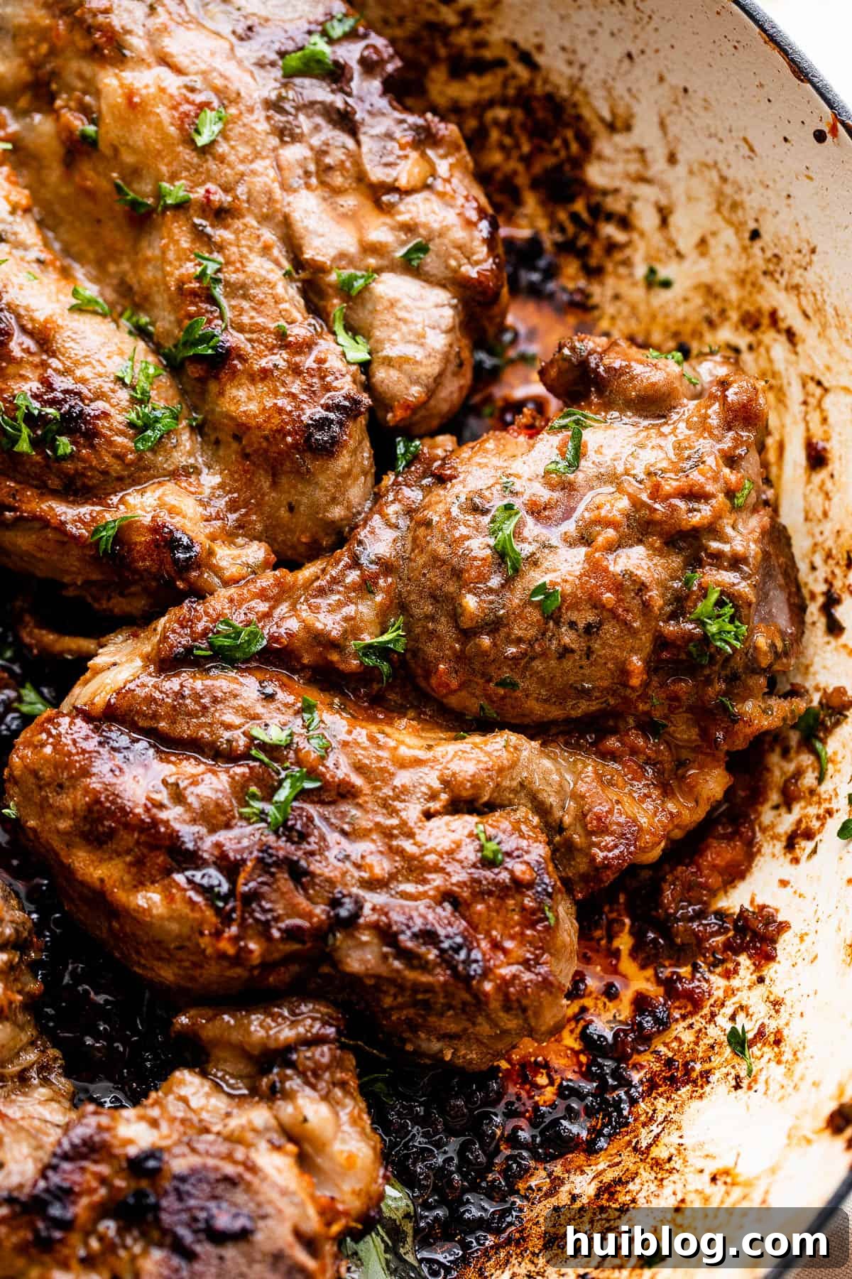Close-up of lamb shoulder chops searing in a white cast iron skillet, developing a perfect crust.