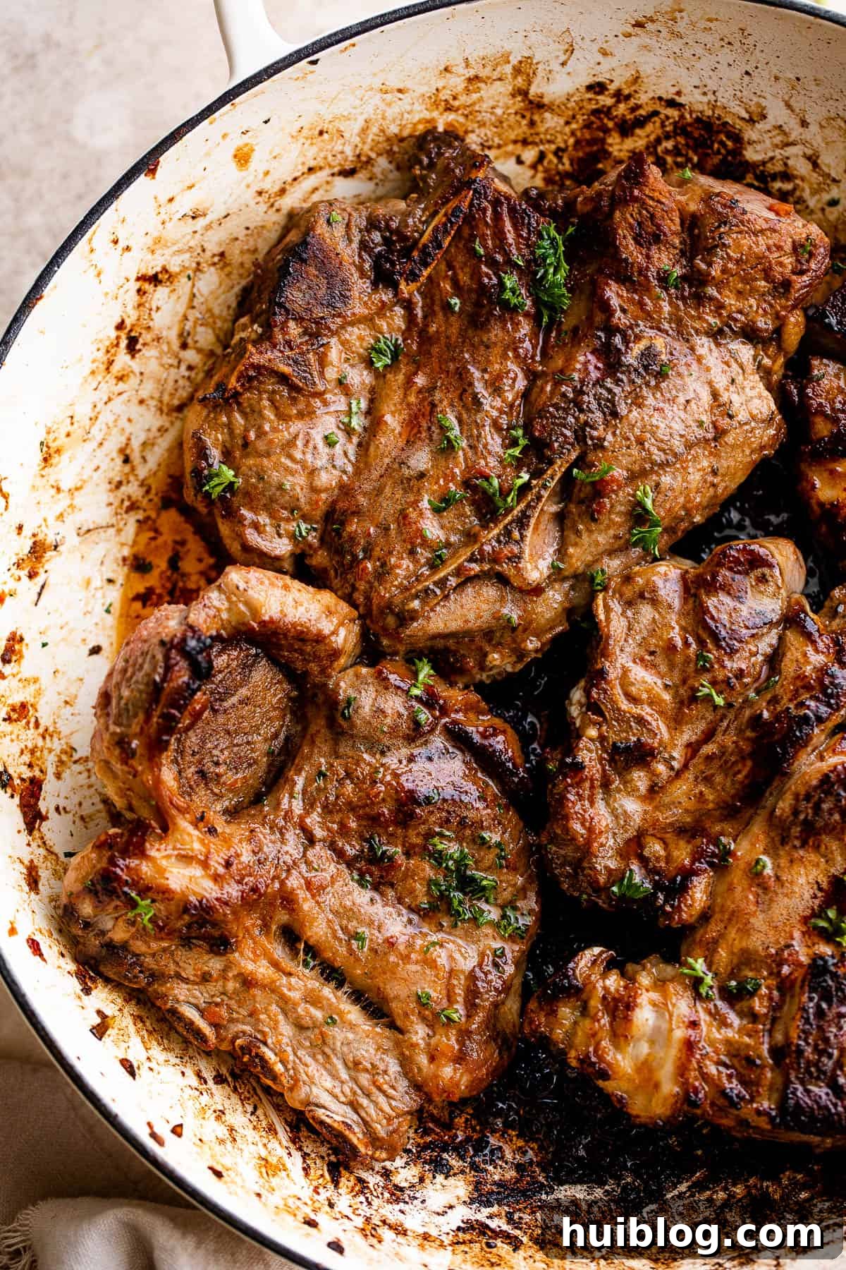 Cooking several lamb chops in a large skillet, showing the golden-brown crust forming.