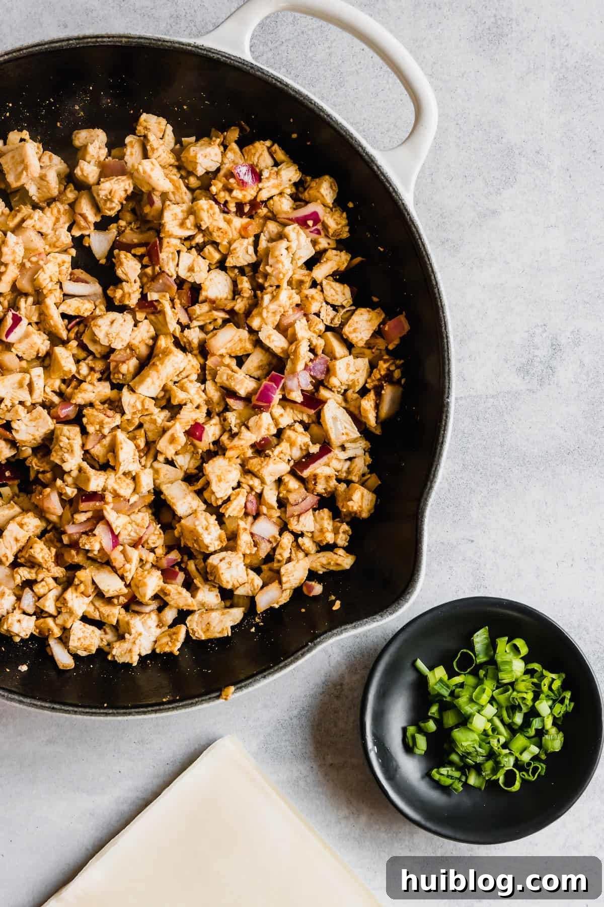 Cheesecake Factory Inspired Tex-Mex Egg Rolls 5 A Skillet with Spices, Diced Chicken, and Onions Next to a Dish of Chopped Scallions