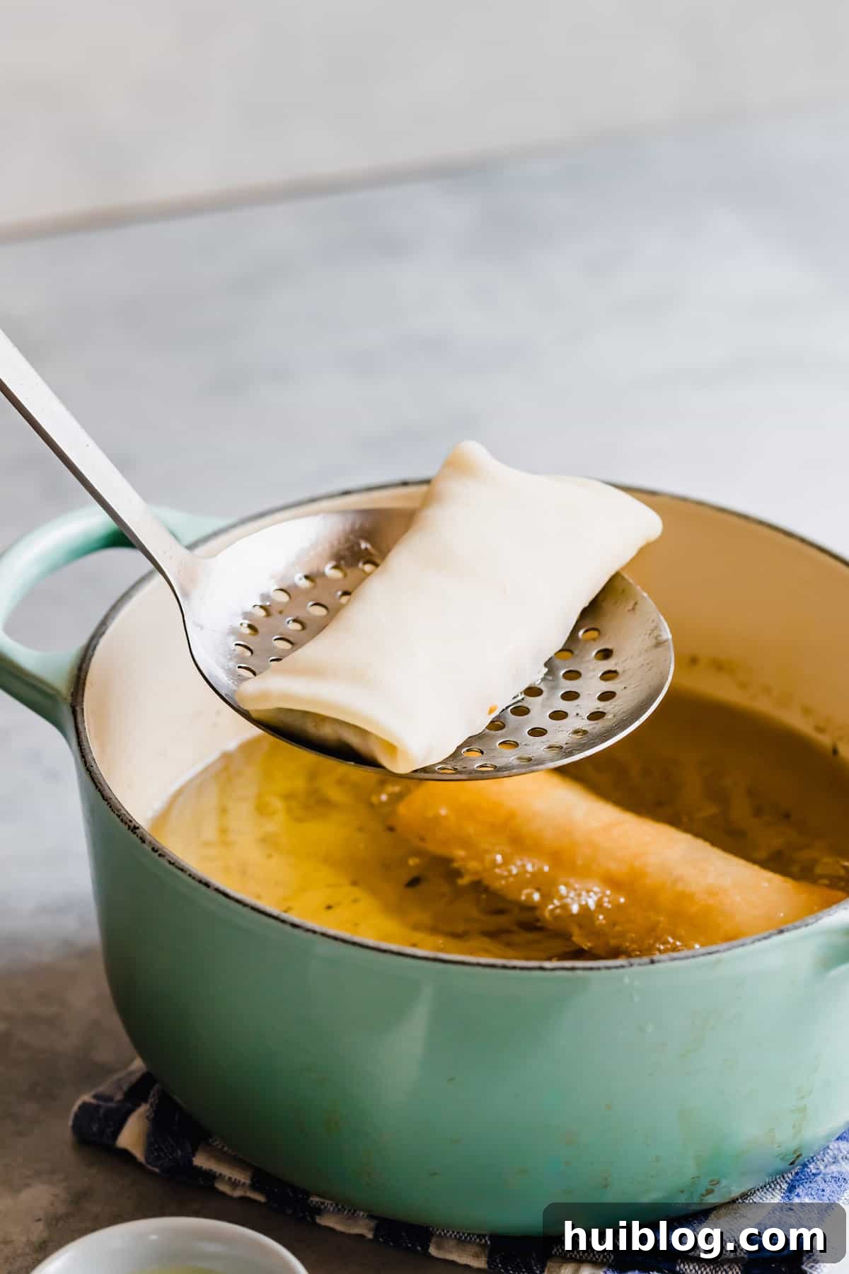 Cheesecake Factory Inspired Tex-Mex Egg Rolls 8 A Slotted Spoon Holding an Uncooked Egg Roll Over a Teal Frying Pan