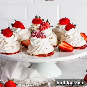 Mini pavlovas on a cake plate topped with whipped cream and strawberries