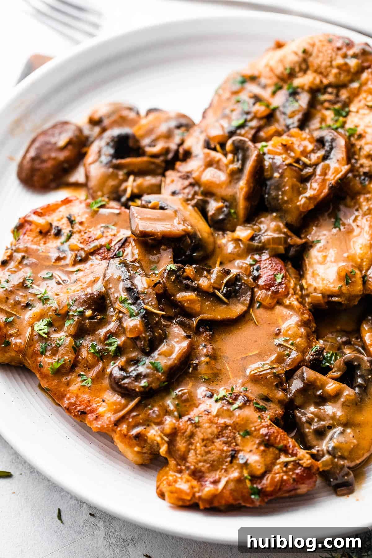 Effortless Instant Pot Pork Chops 3 two bone in pork chops served on a white plate and topped with creamy mushroom gravy