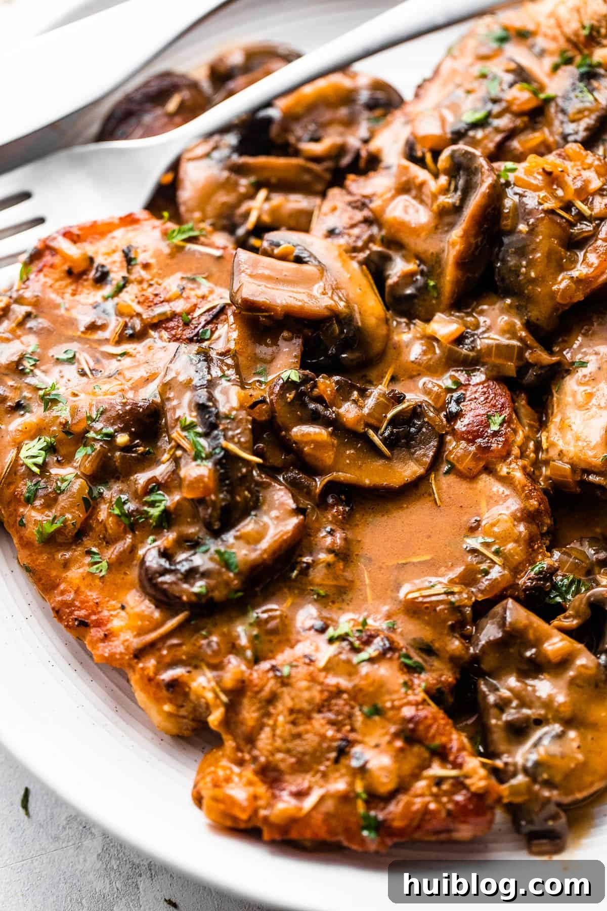 Effortless Instant Pot Pork Chops 6 two bone in pork chops served on a white plate and topped with creamy mushroom gravy