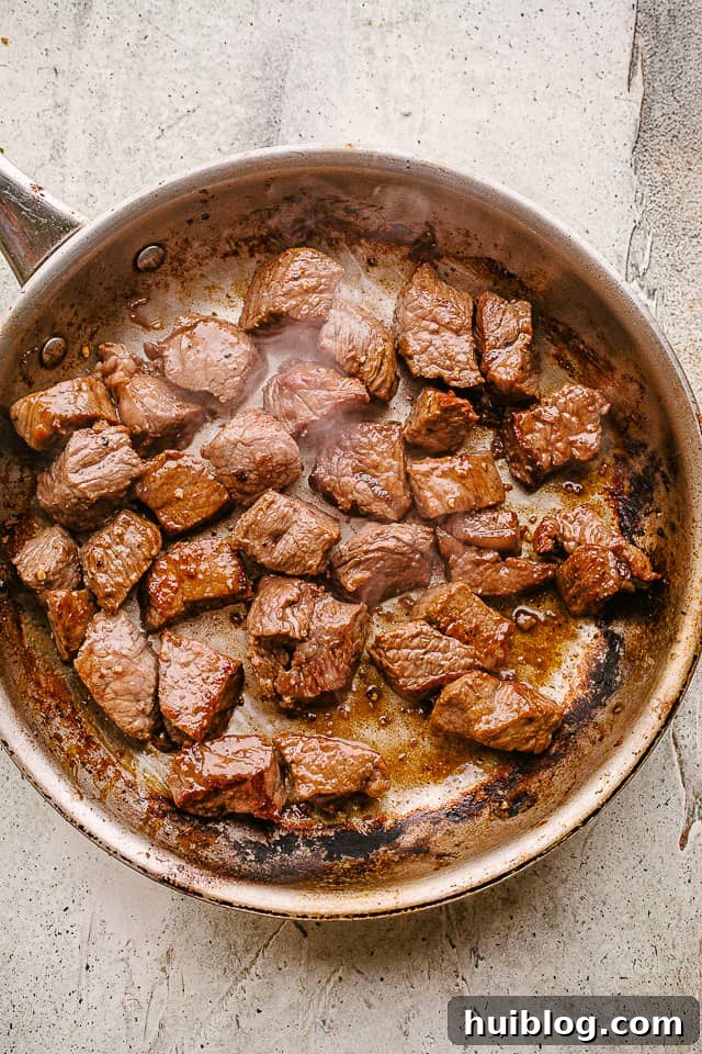 Beef tips being seared in a hot skillet until golden brown.
