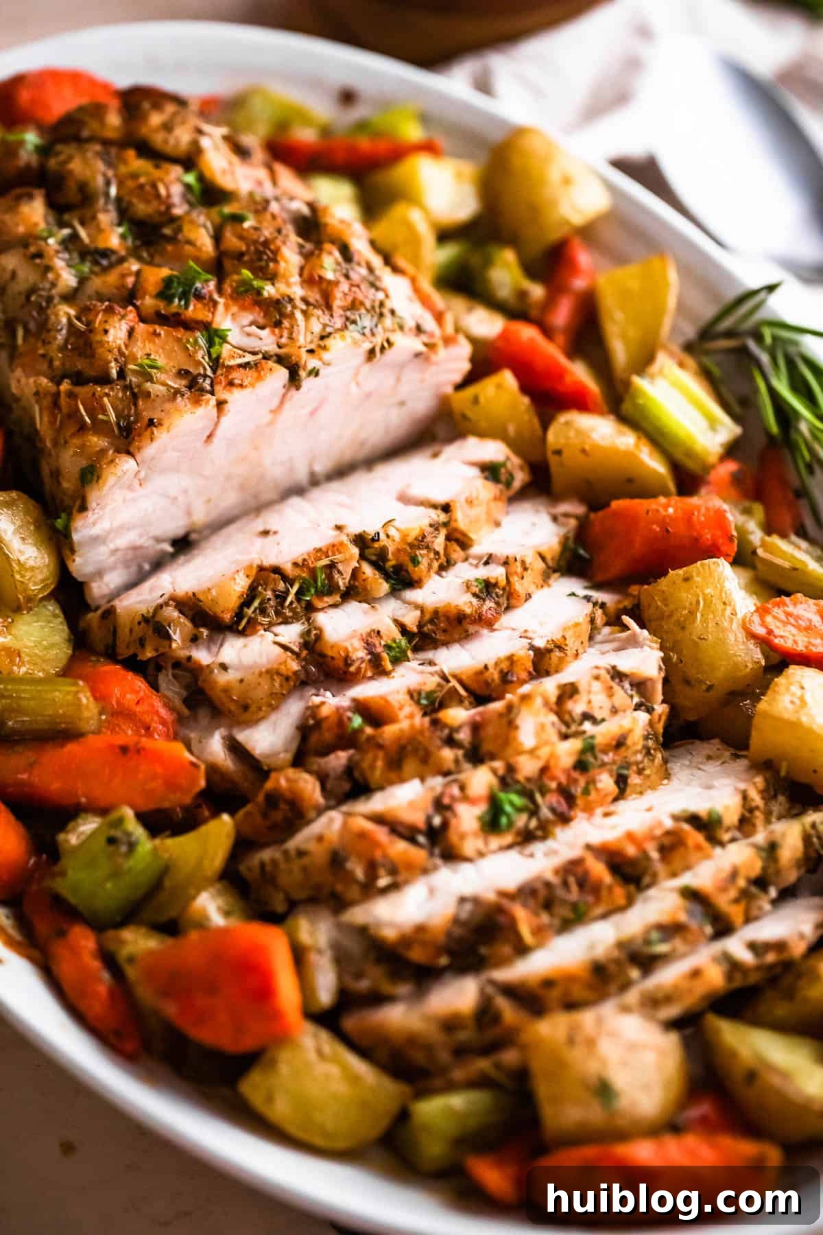 Herb Roasted Pork Loin with Root Vegetables 2 Side shot of an oval plate showcasing a perfectly cooked and sliced pork loin roast, artfully arranged with a colorful assortment of roasted vegetables around it.