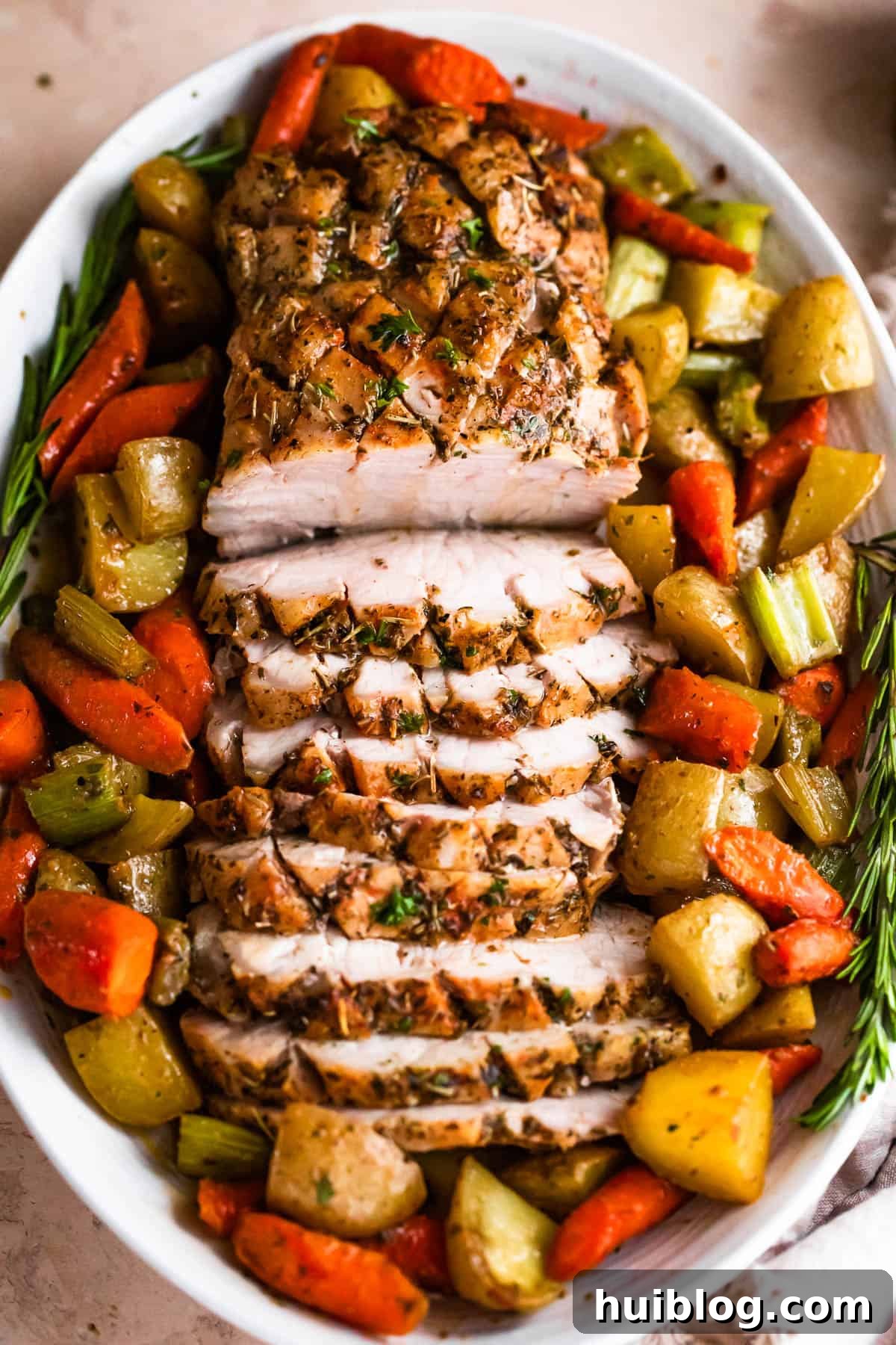 Herb Roasted Pork Loin with Root Vegetables 3 Overhead shot of an oval plate featuring a beautifully cooked and sliced pork loin roast surrounded by a colorful array of roasted carrots, celery, and potatoes.