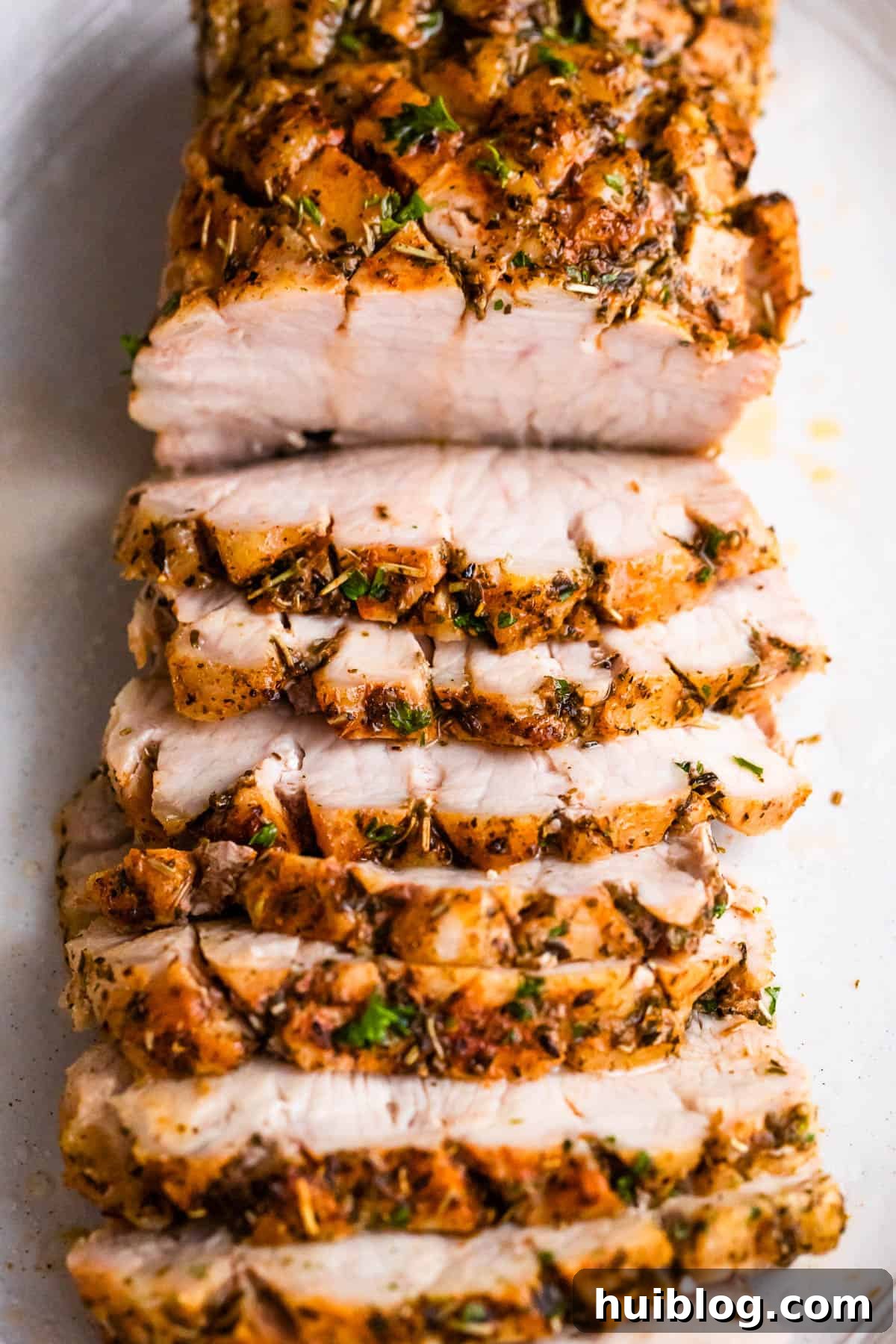Herb Roasted Pork Loin with Root Vegetables 5 Overhead shot of a cooked and beautifully sliced pork roast set against a pristine white background, showcasing its tender texture.