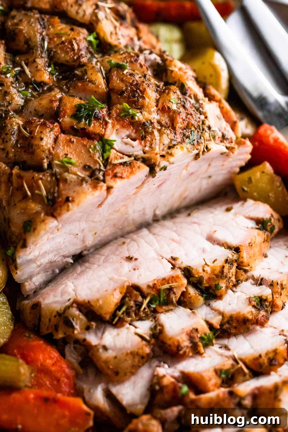Herb Roasted Pork Loin with Root Vegetables 6 Close-up shot of baked pork loin roast, expertly sliced and served with a vibrant array of roasted vegetables on a white plate.