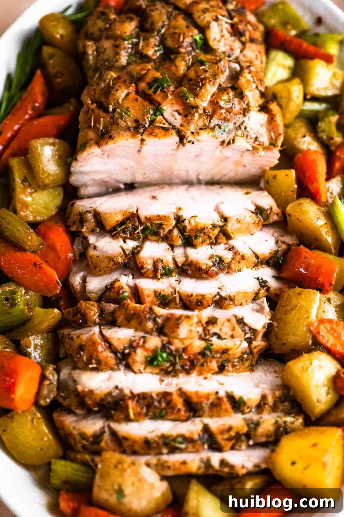 Herb Roasted Pork Loin with Root Vegetables 7 Overhead shot of an oval plate with a perfectly cooked and sliced pork loin roast, beautifully arranged with an assortment of roasted vegetables around it.