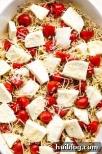 Zesty Caprese Chicken Bake 10 Caprese chicken casserole in a white baking dish topped with fresh mozzarella chunks and cherry tomatoes.