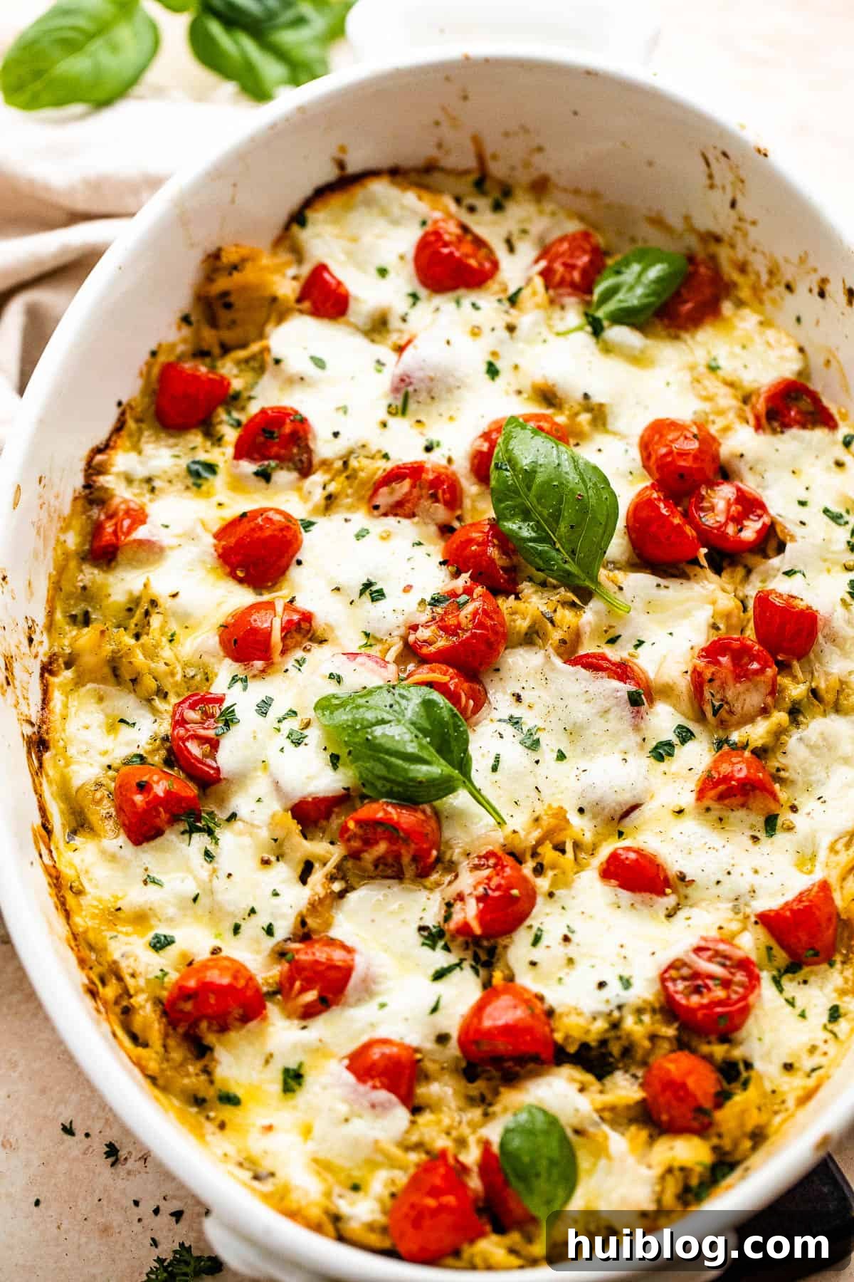 Zesty Caprese Chicken Bake 3 A close-up of Caprese Chicken Casserole in a white baking dish garnished with fresh basil and cherry tomatoes, highlighting the melted cheese.