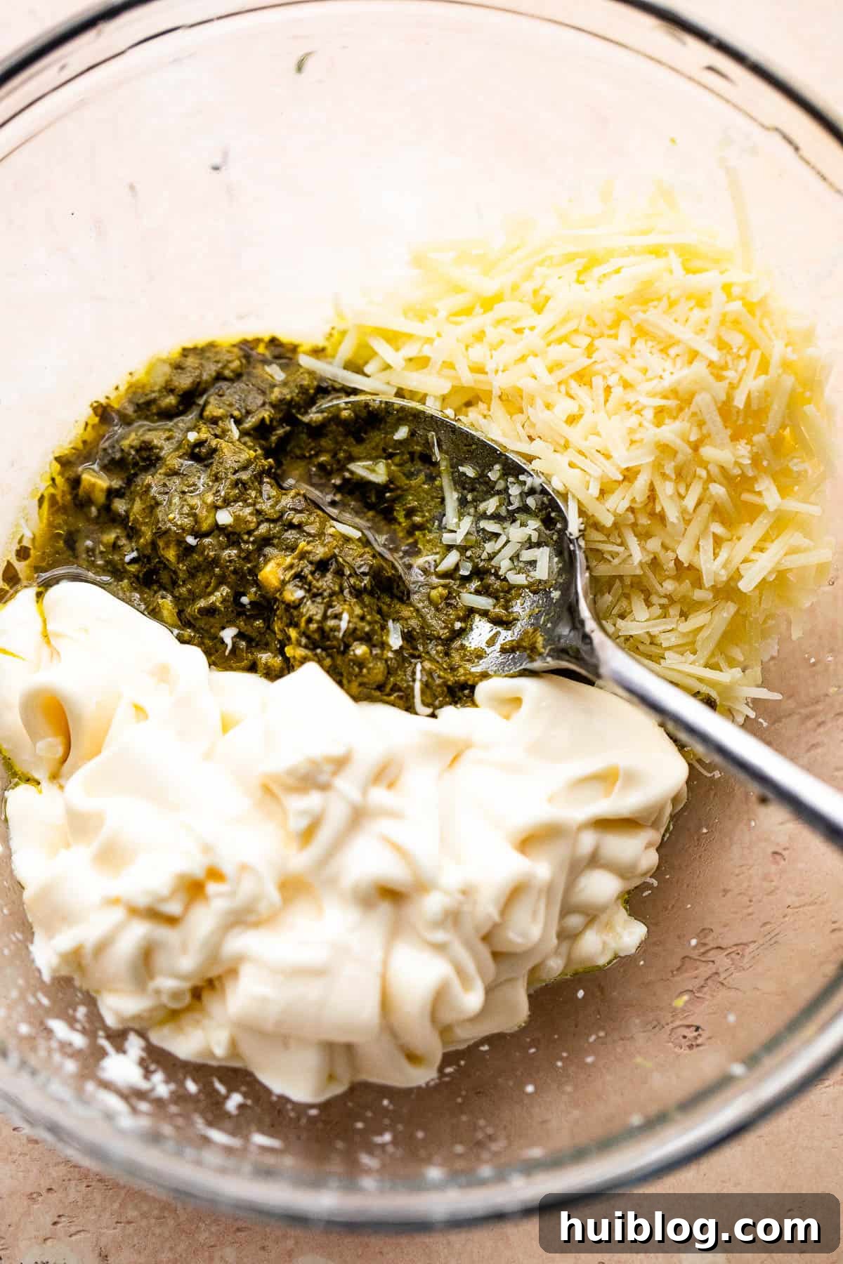 Zesty Caprese Chicken Bake 4 Mixing basil pesto, mayonnaise, and shredded parmesan cheese in a bowl to create the creamy sauce for the Caprese chicken casserole.
