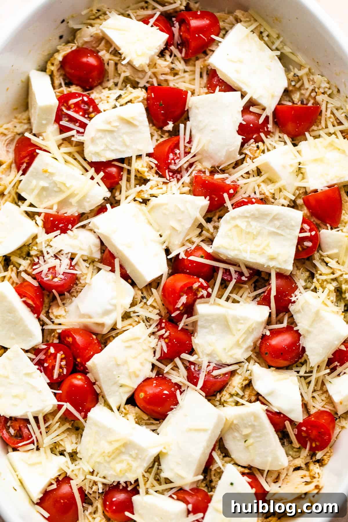 Zesty Caprese Chicken Bake 5 Caprese Chicken Casserole in a white baking dish topped with fresh mozzarella chunks and cherry tomatoes, ready for baking.
