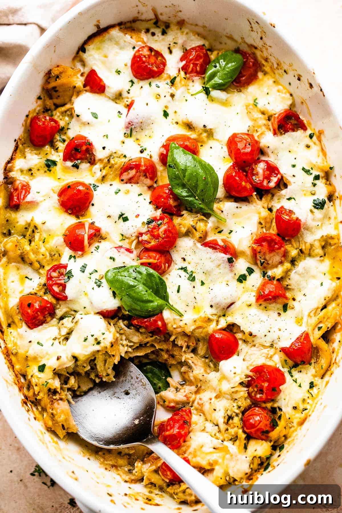 Zesty Caprese Chicken Bake 6 A serving spoon lifting a portion of Caprese Chicken Casserole from the baking dish, showing the cheesy, saucy interior.