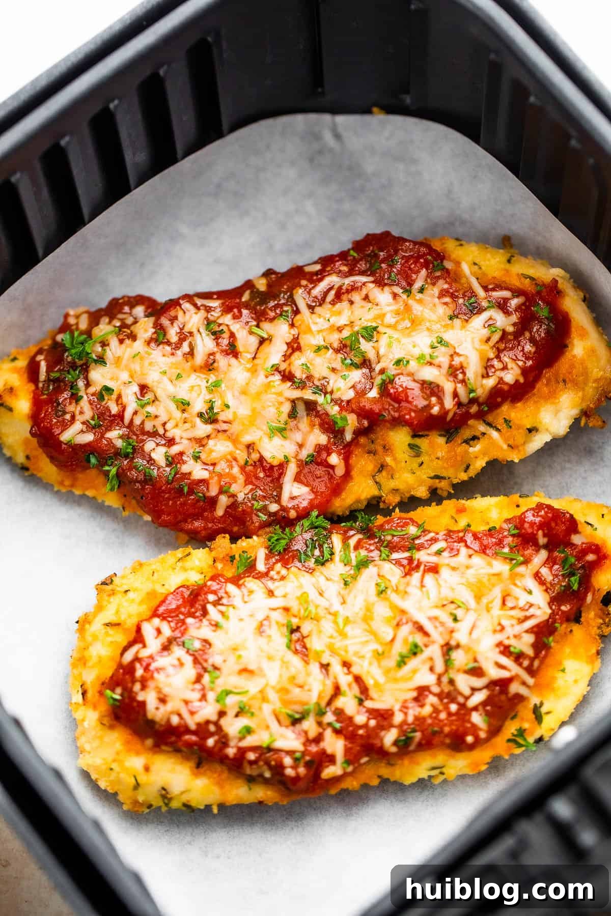 Ultimate Air Fryer Chicken Parmesan 2 Two Pieces of Breaded, Partially Cooked Chicken Being Topped with Marinara and Shredded Parmesan Cheese