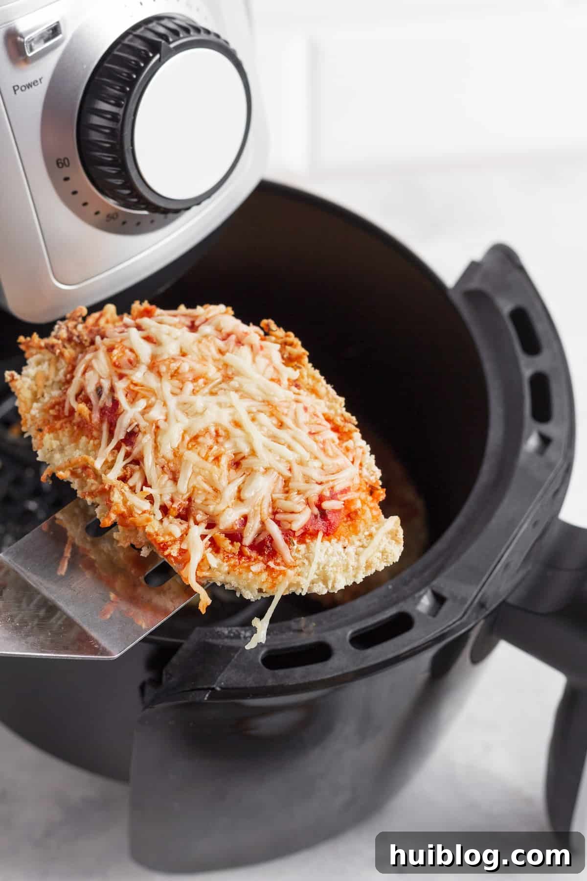 Ultimate Air Fryer Chicken Parmesan 4 A Piece of Chicken Parm on a Metal Spatula Hovering Above an Air Fryer Basket