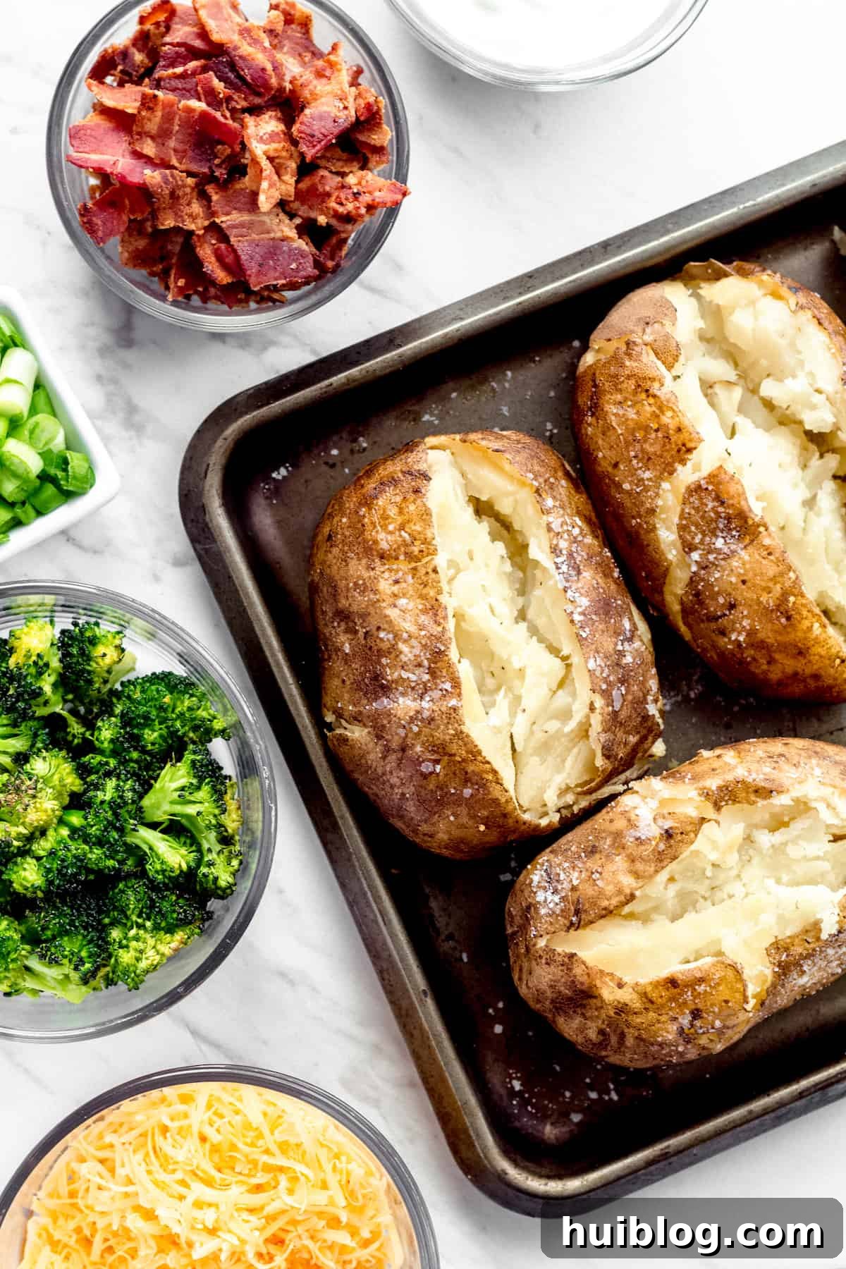 Three Instant Pot Baked Potatoes Beside Bowls of Cheese, Broccoli, Bacon, Chopped Green Onions and Sour Cream