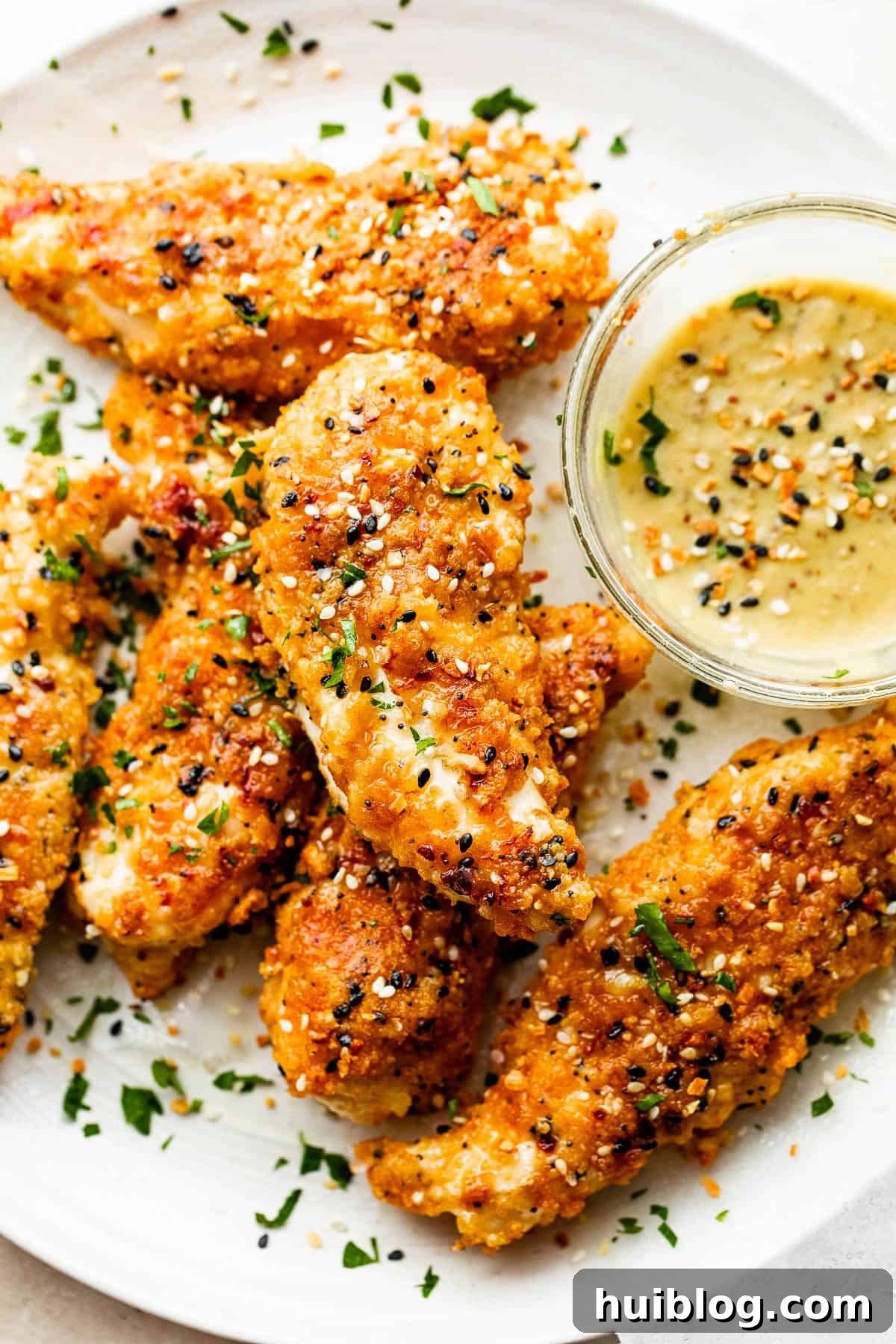 close up of six Everything Bagel Chicken Tenders arranged on a round plate and served with honey mustard dipping sauce