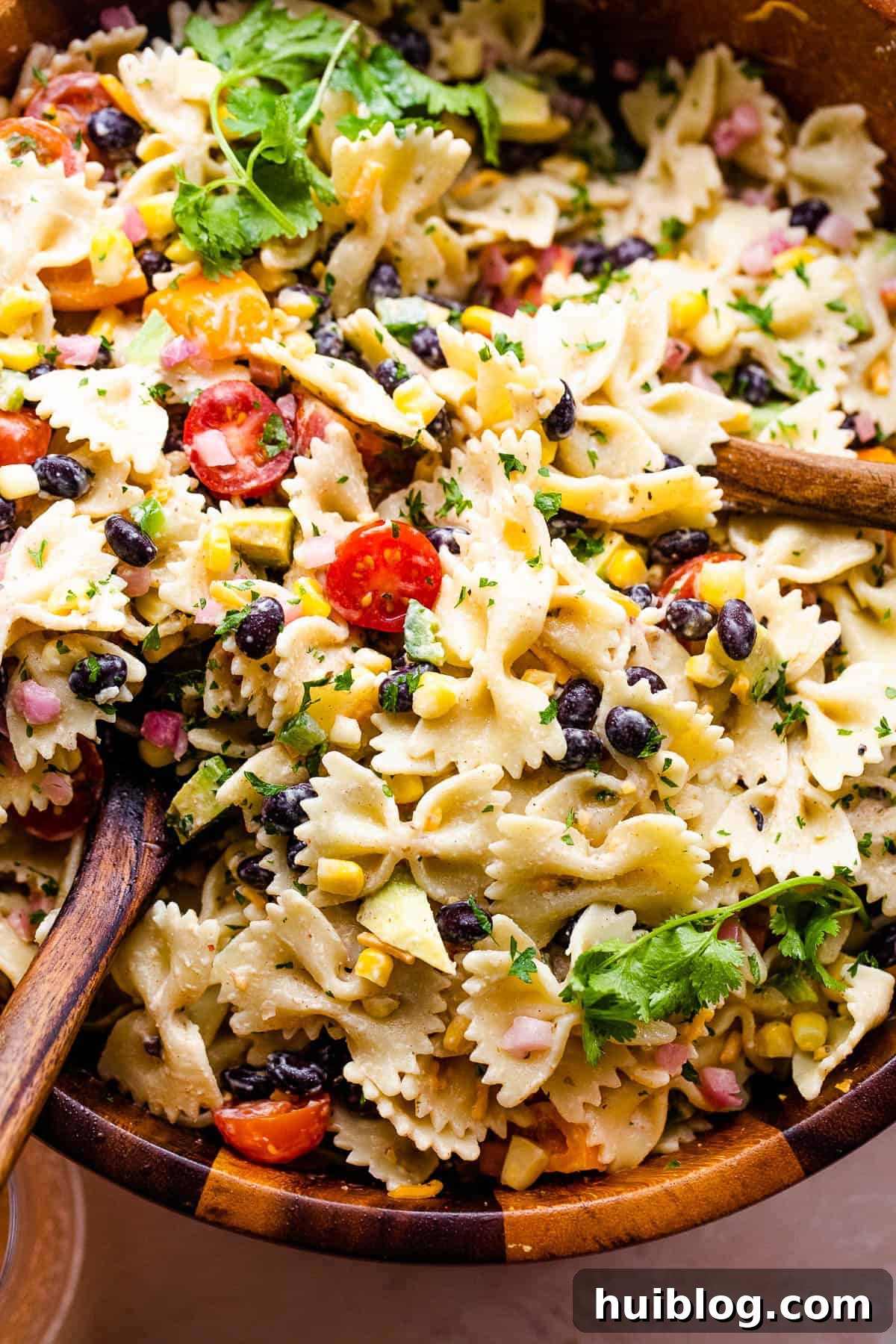 Vibrant Fiesta Pasta Medley 3 Close-up shot of Fiesta Pasta Salad showcasing the vibrant mix of corn, black beans, avocado, and tomatoes, served in a wooden bowl with two spoons.