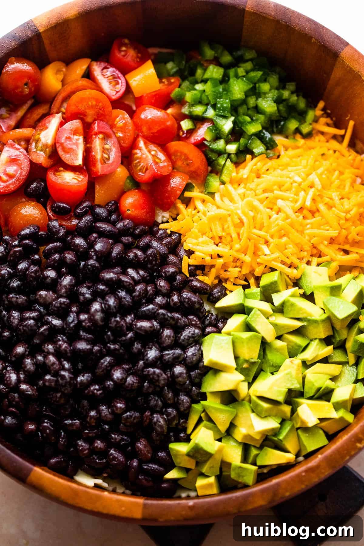Vibrant Fiesta Pasta Medley 4 Various ingredients for Fiesta Pasta Salad in separate wooden bowls, including chopped tomatoes, diced avocado, shredded cheddar cheese, and black beans.